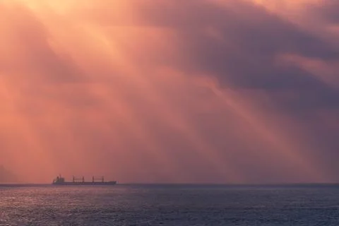 Sunrays on the ocean with freighter ship Stock Photos