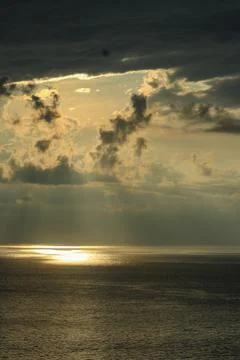 Sunrays Piercing Dark Storm Clouds Over Calm Ocean Sunset Stock-Fotos