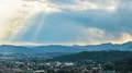 Sunrays shining through clouds over city surrounded by mountains, time-lapse 4k or 4k+ Resolution