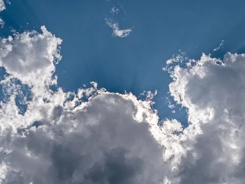 Sunrays shining through white clouds on blue sky background Stock Photos
