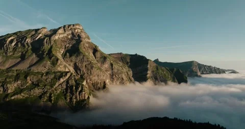 Sunrise aerial showing dramatic alpine cliffs above dense cloud inversion in Stock Footage 316764773