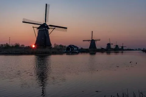 Sunrise on the alignment of windmills reflected on the calm water in the long Фото