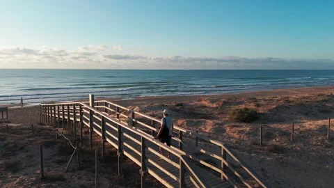 Sunrise beach stroll: man in white hat, light shirt, shorts, and flip-flops.. Stock Footage 283973408