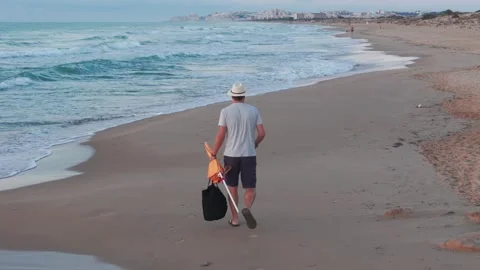 Sunrise beach stroll: man in white hat, light shirt, shorts, and flip-flops.. Stock Footage 284871134
