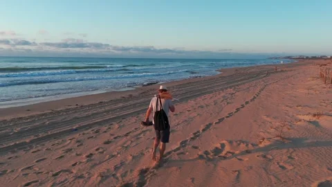 Sunrise beach stroll: man in white hat, light shirt, shorts, and flip-flops.. Stock Footage 286814407