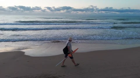 Sunrise beach walk: man in white hat, light shirt, shorts, and flip-flops c.. Stock Footage 282253984