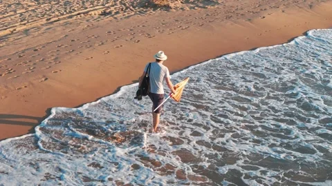 Sunrise beach walk: man in white hat, light shirt, shorts, and flip-flops c.. Stock Footage 282710370