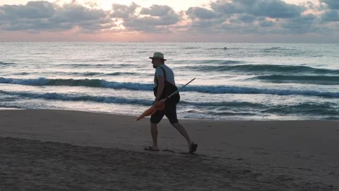 Sunrise beach walk: man in a white hat, light shirt, shorts, and flip-flops.. Stock Footage 283723898