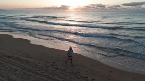 Sunrise beach walk: man in white hat, light shirt, shorts, and flip-flops c.. Stock Footage 283973665