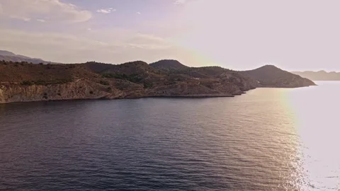 Sunrise brings light over calm water and mountains near the coast Stock Footage 340191423