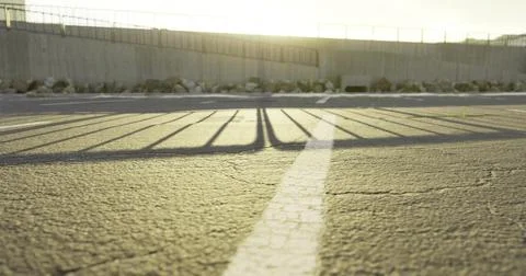 Sunrise casts long shadows over cracked pavement in an open area Stock Illustration