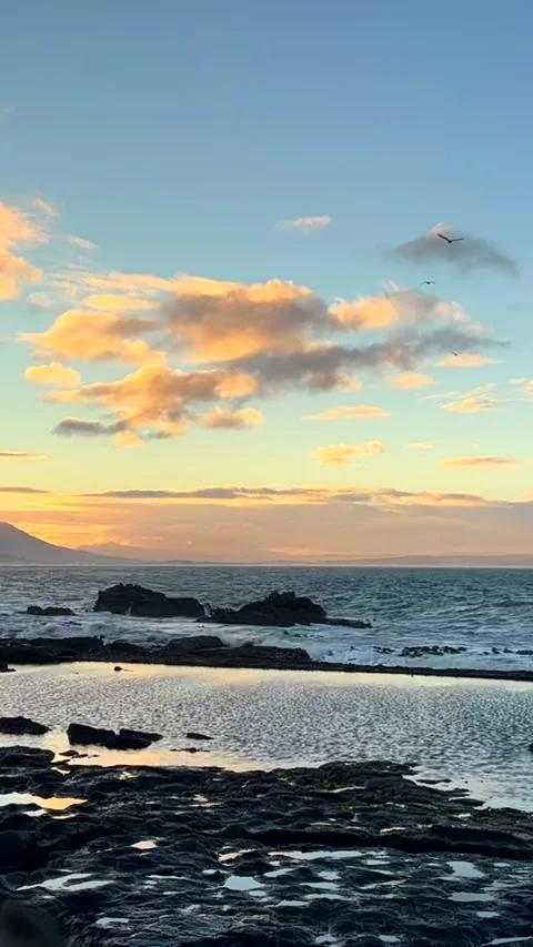 Sunrise clouds fly over ocean viewed over Hermanus tide pool Stock Footage 346118111