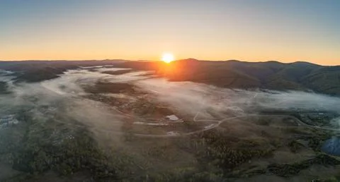 Sunrise mist settling over a tranquil rural valley, revealing a winding river Stockfoto's