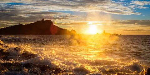 Sunrise or sunset at the beach with waves and hilly seashore Stock Photos
