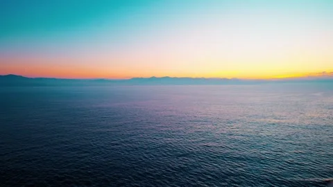Sunrise over calm ocean with distant mountain horizon Video stock 337298224