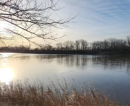 Sunrise over calm river with reflections and winter trees Stock Photos