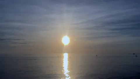 Sunrise over calm sea with distant fishing boats and paddle boarders on Video stock 337777090