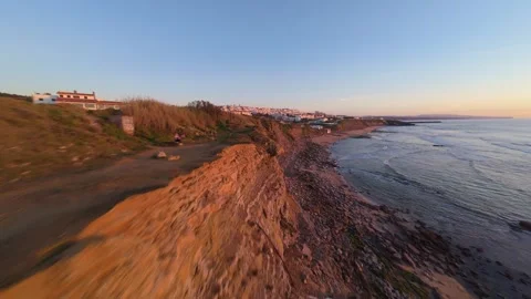 Sunrise over cliffside town, ocean waves gently meet sandy shore Stock Footage 344564111