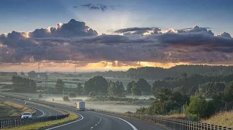 Sunrise over a misty highway with dramatic clouds and sunbeams breaking throu Fotos Stock