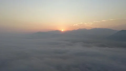 Sunrise over misty mountain range with soft cloud layer and warm sky Stock Footage 344815154