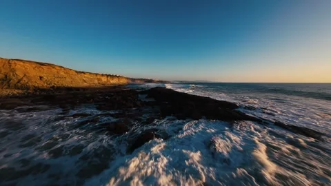 Sunrise over rugged coast with waves breaking on black rocks Stock Footage 339788666