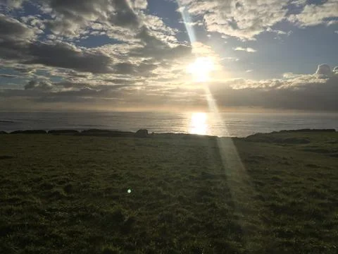 Sunrise Over Tranquil Ocean Waves Reflecting Golden Light on Soft Grass Foto stock