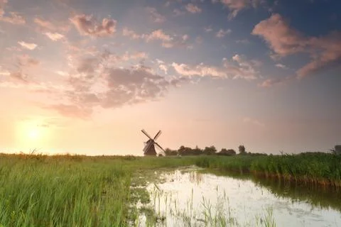 Sunrise over windmill by river Foto stock