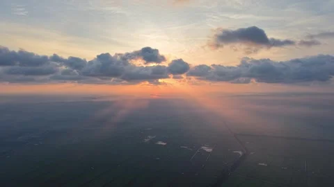 Sunrise peaks through clouds over fields and water 動画素材 333038699