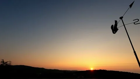 Sunrise from a rooftop with a rotating metal wind vane in the shape of a Stock Footage 280027341