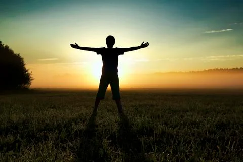 Sunrise scene. Silhouette of a boy standing in the field. Stock Photos