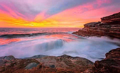 Sunrise sun rays light up the sky and reflect in the ocean and rocks Stock Photos