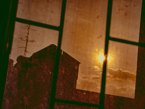 Sunrise Through Dusty Window Screen with Rooftop Silhouette, Urban Morning .. 库存照片