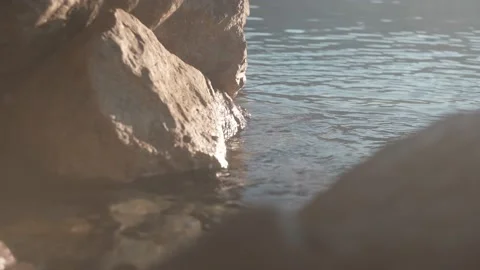 The sun's rays are reflected in the water that washes the stones on the beach Stock Footage 220668129