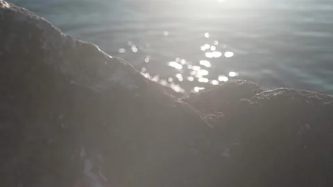 The sun's rays are reflected in the water that washes the stones on the beach Stock Footage 220668151