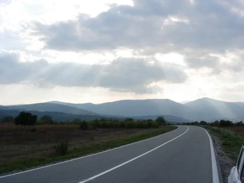 Sun's rays break through the cloud above the road Stock Photos
