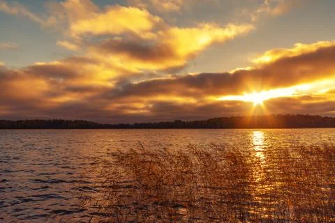 Sun's rays make their way through the clouds above the lake at sunset. Beauti Stock Photos