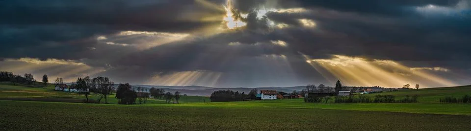 The sun's rays pierce the clouds over the agricultural field Stock Photos