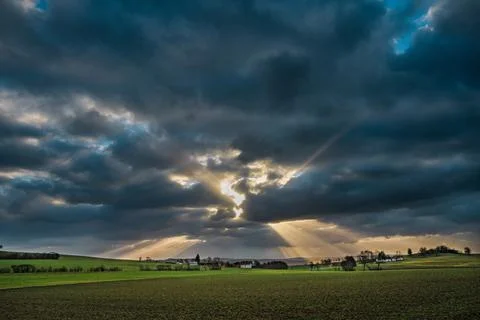The sun's rays pierce the clouds over the agricultural field Stock Photos