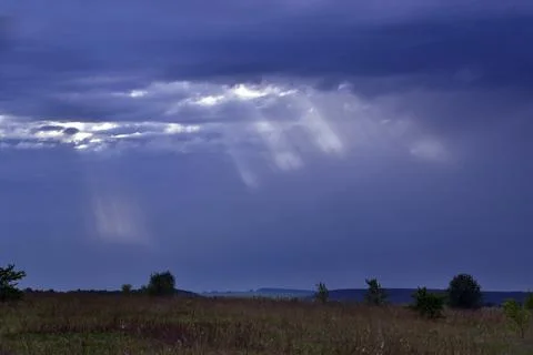 The sun's rays through the clouds illuminate the streams of summer rain in th Foto stock
