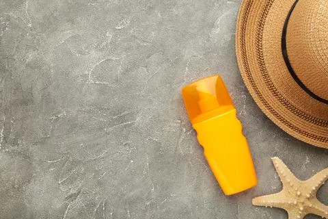 Sunscreen bottle with hat and shells on grey background. Cosmetics for safe s Stock Photos