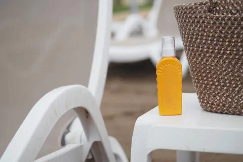 Sunscreen bottle next to basket on poolside chair at sea beach Stock Photos