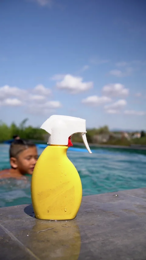 Sunscreen Spray Bottle Rests Poolside as Child Jumps Into Water Stock Footage 343907207