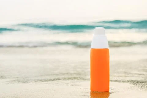 Sunscreen spray in orange bottle on the sand against the backdrop of sea wave Stock Photos
