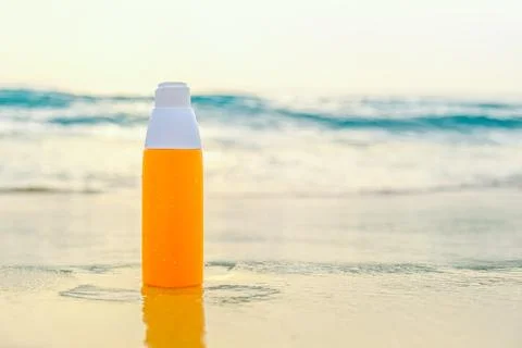Sunscreen spray in orange bottle on the sand against the backdrop of sea wave Stock Photos