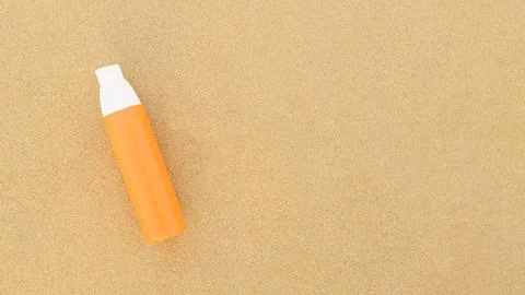Sunscreen spray in orange bottle on a sandy background Stock Photos