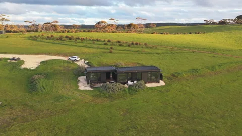 Sunset aerial of a container home in the rolling green coastal hills of Stock Footage 328089484