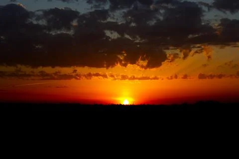 Sunset against dark blue clouds. Black field at sunset. Stock Photos