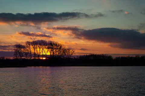 Sunset and clouds behind the trees on the lake Stock Photos