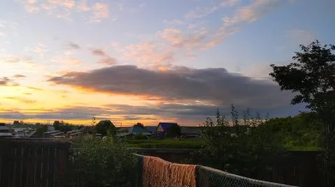 Sunset and clouds in the evening sky over the houses in the Russian village Stock Photos