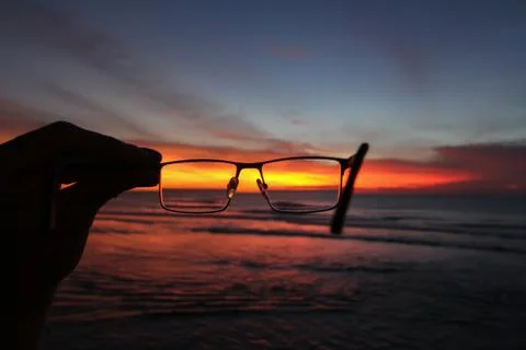 Sunset and ocean through glasses in one hand Stock Photos